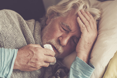 Starší pán s chřipkou ležící v posteli